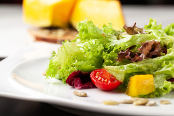 European Italian salad of lettuce, cherry tomatoes, pumpkin, edible pumpkin flowers, and pumpkin seeds, in a white plate. Copy space, selective focus