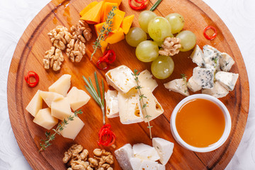 Cheese plate. Delicious cheese mix with walnuts, honey, grapes on wooden table. Tasting dish on a wooden plate. Food for wine.