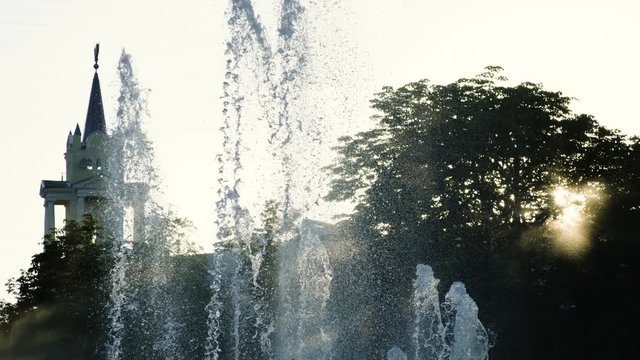 Medium shot of water drops of fountain in summer park at sunset. 4K