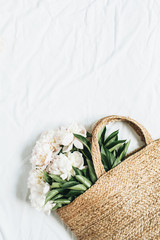 Straw bag with white peony flowers on white background. Flat lay, top view summer floral concept.