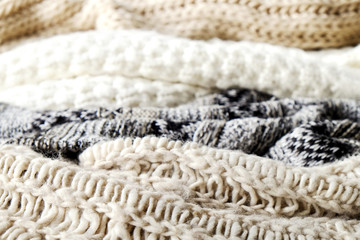 Fototapeta na wymiar Bunch of knitted warm pastel color sweaters with different knitting patterns laid in messy pile, clearly visible texture. Stylish fall / winter season knitwear clothing. Close up, copy space for text.