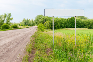 Straight road with white empty sign on roadside at the entrance to the city against beautiful summer landscape background. Bolshaya Doroga village, Tambovsky region, Russia.