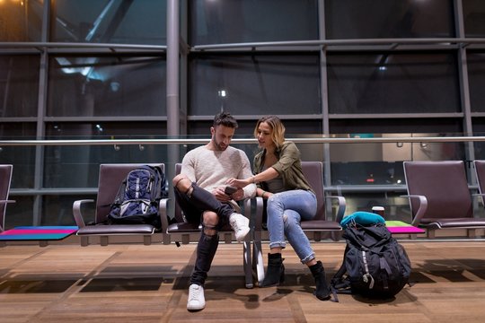 Young couple using cell phone while sitting at airport