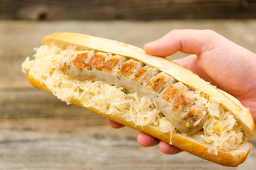 Young man holding a grilled sausage sandwich with sour cabbage. Delicious bratwurst sandwich with sauerkraut