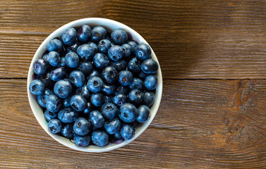 Summer close-up of blueberries on vintage wooden background. Freshly picked berries in white bowl. Top view of blueberries on a rustic workplace. Bilberry on wooden background. Blueberry antioxidant.