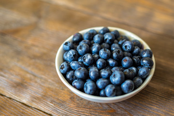 Blueberries on vintage wooden background. Freshly picked berries in white bowl. Ripe and juicy fresh picked bilberries close up. Copyspace for your text. Concept for healthy eating and nutrition.