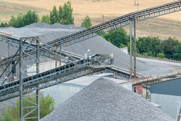 Fototapeta premium Belt conveyors and mining equipment in a quarry. Stone quarry with conveyor belts and piles of stones. Quarrying of stones for construction works.