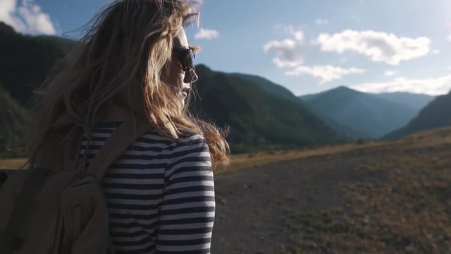 portrait of a tourist girl close-up. A traveler with a backpack and wearing sunglasses walks through the mountainous terrain.