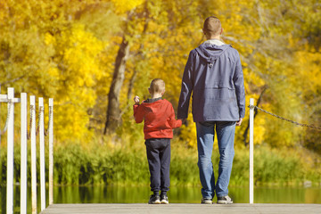 Father and son are standing on the pier. Autumn, sunny. Back view