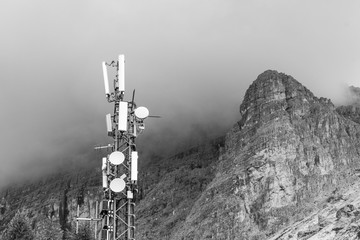 Transmitter station on top of a mountain with storm clouds gathering around a mountain peak in the...
