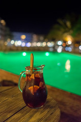 Sangria carafe on the wooden table at night by the pool