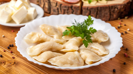 The concept of Ukrainian cuisine, vareniki with potatoes, with sour cream in a white plate on the...