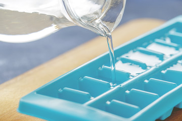 Pouring water into ice cube tray on the kitchen table. - 215804402