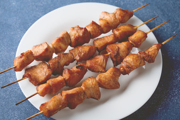 Baked chicken on bamboo skewers on white plate on blue background.