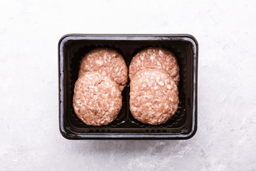 Raw ground meat patties in plastic box on a white marble table. Fresh beef and pork mince