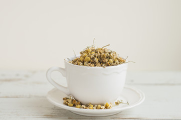 White tea cup with dried chamomile flowers on wooden table. Healthy herbs