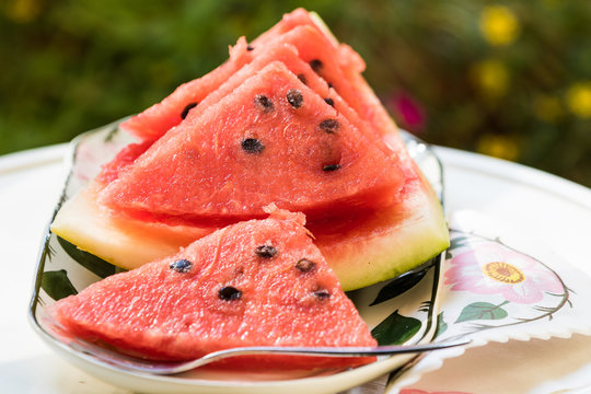 Slices of red watermelon on the white table surface and flowers in the garden