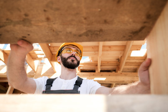 The man is a builder on the roof of a wooden frame house.