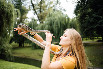 beautiful blonde girl is holding a snake in her hands. Contact the zoo.