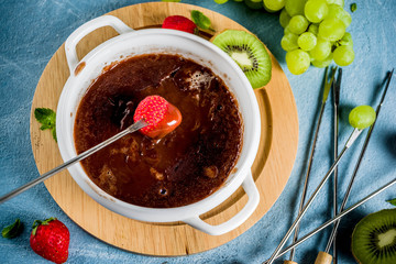 Sweet fruity chocolate fondue dessert with strawberry, grape and kiwi, light blue concrete background copy space