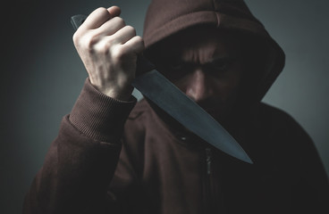 Criminal hooded man showing knife on dark room. - Powered by Adobe