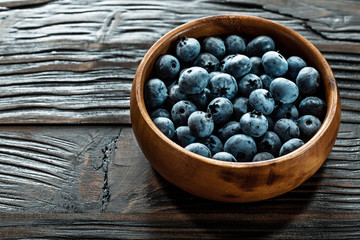 Blueberries in round wooden bowl on wood board