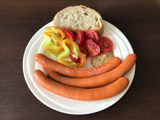 Hot dogs with pepper, tomatoes, mustard and bread on plate