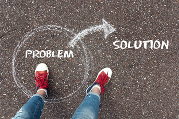 Feet  in red sneakers standing inside problem circle and outward arrow chalky on the asphalt.