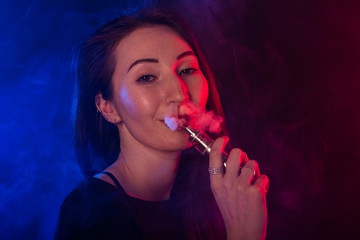 Obraz premium Young woman smoking vape or e-cigarette in neon light