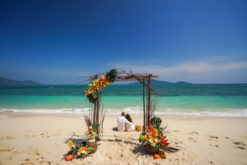 A pair of newlyweds are sitting on the sand of a tropical island after registering a wedding in the Traditional Thai arch and marooning.