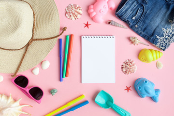 Baby girls' things for the beach. Straw hat, shorts, sunglasses, block with flippers, toys for sand on a pink background. View from above