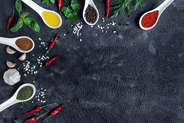 assortment of indian spices and herbs in ceramic spoon on black background, chili peppers and greens.