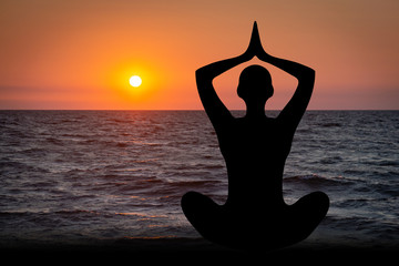 Silhouette of a woman doing yoga exercises on the beach in the sunset