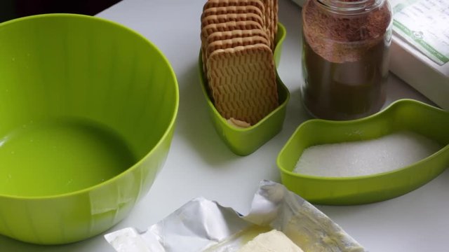 Preparation of chocolate sweets from cocoa and biscuits. On the table are the ingredients. Biscuits, cocoa, butter and sugar in containers.