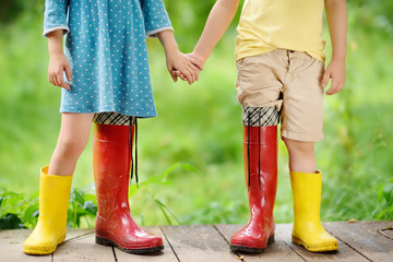 Little children wearing oversized rubber boots holding hands