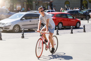 Side view portrait of a young attractive man wearing sunglasses riding on bicycle in city street