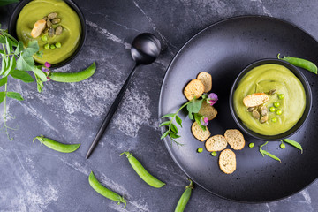 Green pea soup puree with croutons in black bowl.  On dark stone background. flat lay.