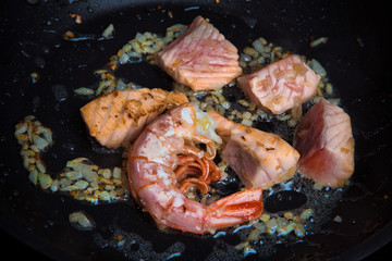 Fototapeta na wymiar pieces of salmon and shrimp are fried in oil in a frying pan