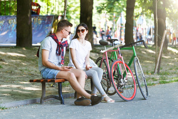 Obraz premium Young couple in love with bicycle sitting on beanch in the sunny summer park