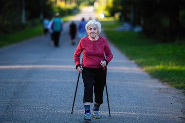 Nordic walking. An elderly woman with ski poles is on the road.