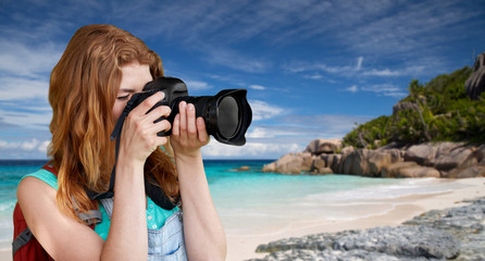 travel, tourism and photography concept - happy young woman with backpack and camera photographing over background of seychelles island beach in indian ocean