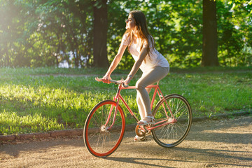 Pretty romantic girl walking with bicycle on the sunset in green summer park