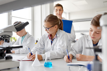 Fototapeta premium education, science and children concept - teacher and students studying chemistry at school laboratory and writing to workbooks