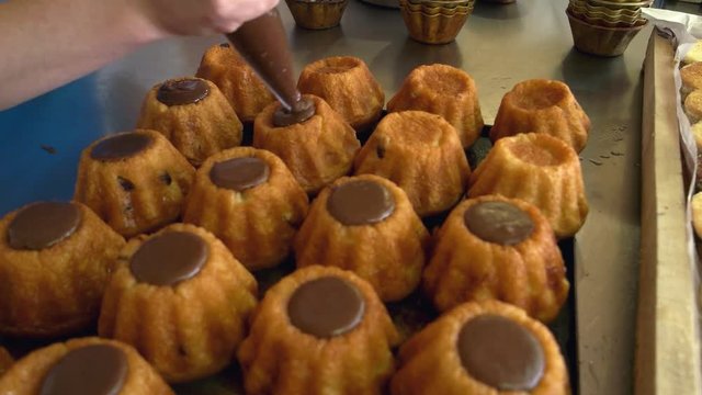 Baker decorating cupcakes with pastry syringe. Confectioner filling cakes with icing using pastry bag. Pastry production at bakery.