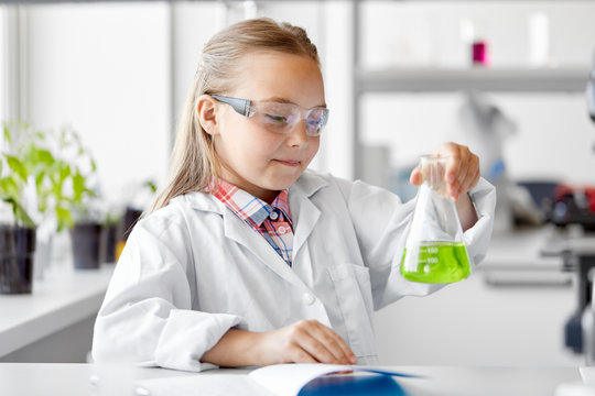 education, science and children concept - girl in goggles with test tube studying chemistry at school laboratory