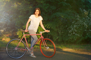 Fototapeta na wymiar Young pretty romantic girl walking with bicycle on the sunset in green summer park