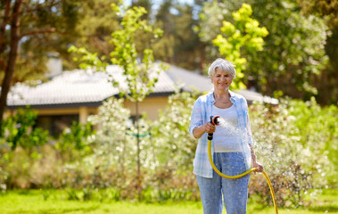 gardening and people concept - happy senior woman watering lawn by garden hose at summer