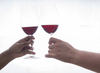 two hands holding wineglasses with red wine