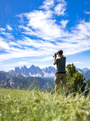 Naklejka na ściany i meble A youg guy taking picture of the Geisler mountains on the plose (Italian Dolomites)