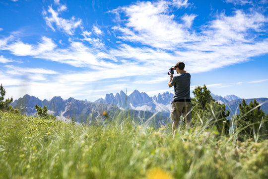 A youg guy taking picture of the Geisler mountains on the plose (Italian Dolomites)